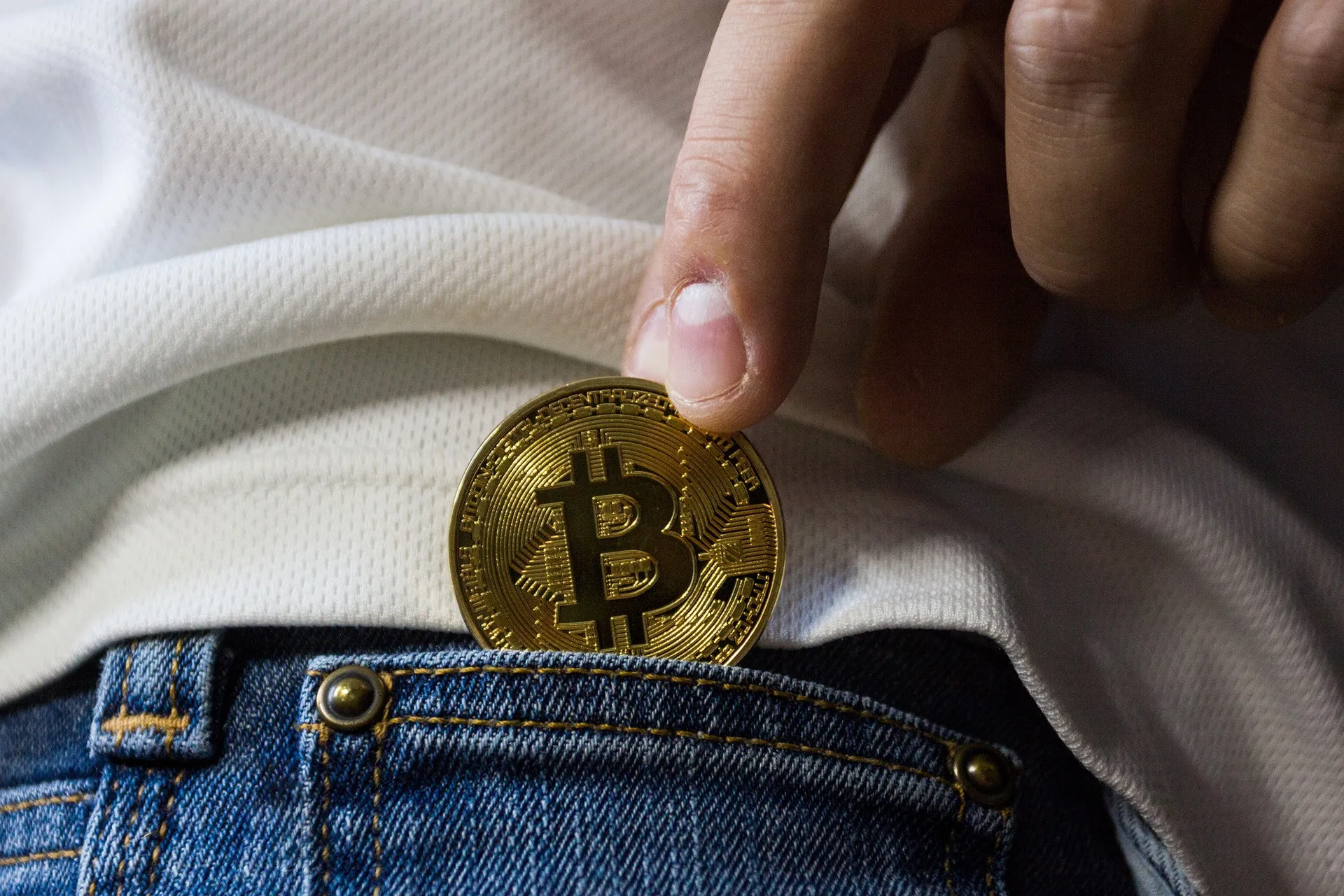 Gold Bitcoin coin being pulled from a jeans pocket