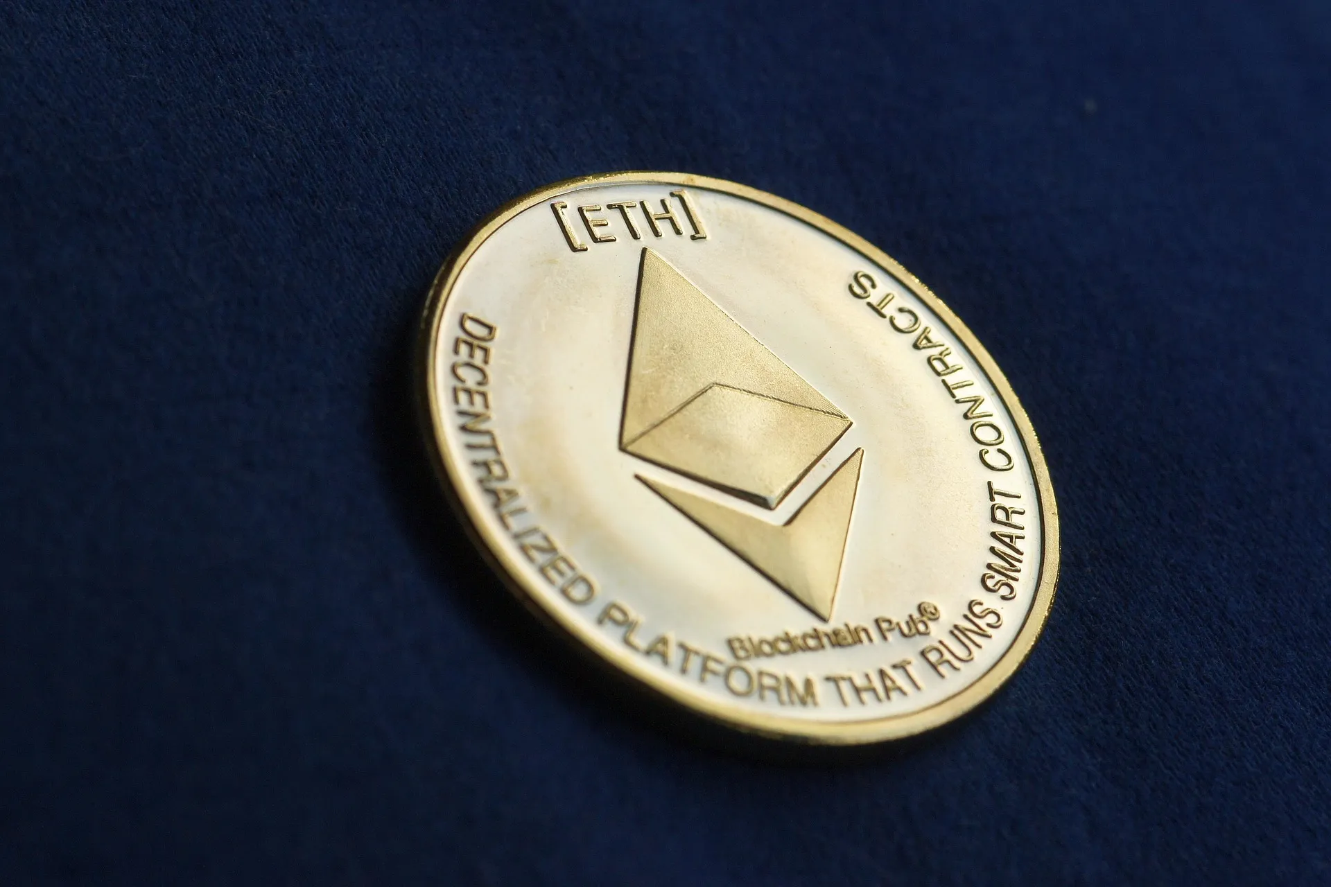 Gold Ethereum coin lying on dark navy fabric