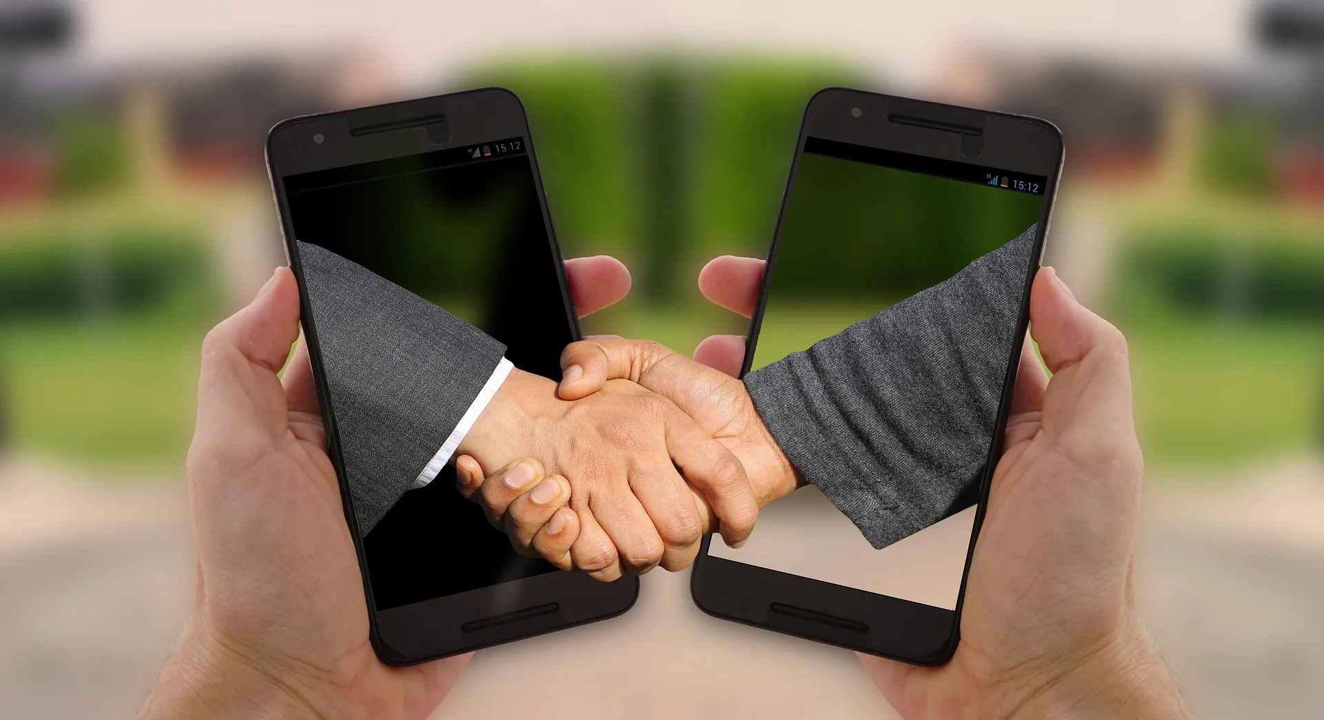 Two people shaking hands through smartphone screens