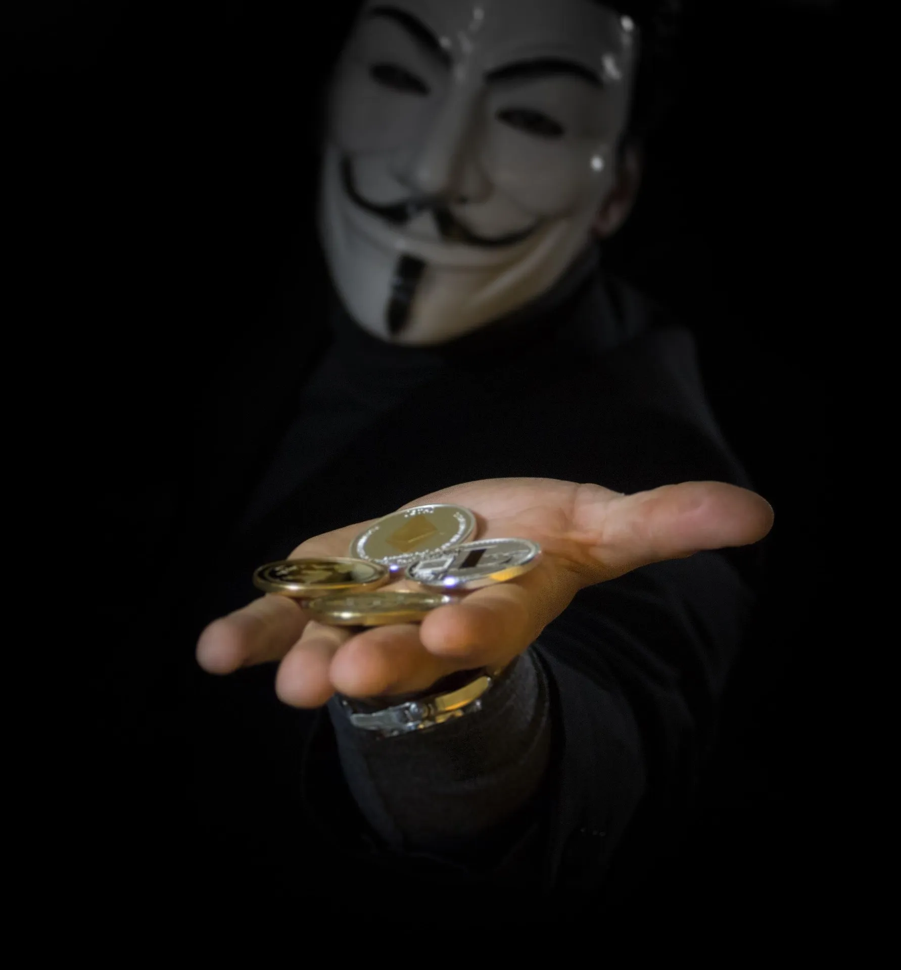 Person in a mask holding out crypto coins
